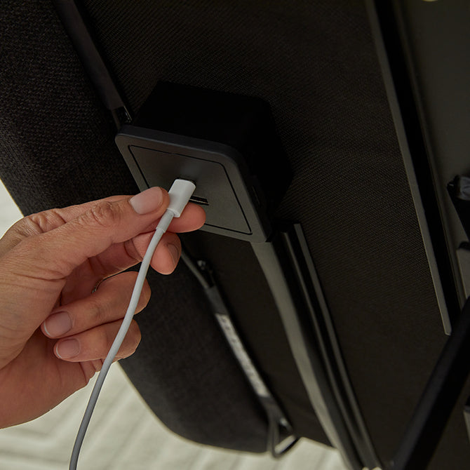 A person plugging a USB cable into the built-in charging port on the side of a Beautyrest adjustable bed frame, highlighting the convenience of charging devices directly from the bed.