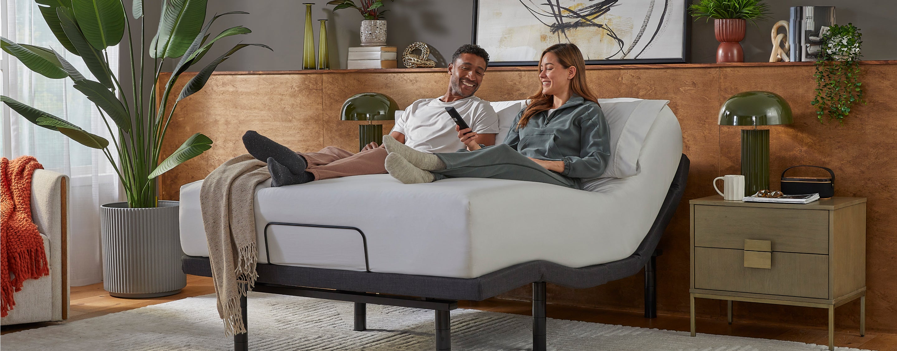 Man and woman sitting on a white beautyrest mattress, sitting on baselogic base with her holding the remote to the base