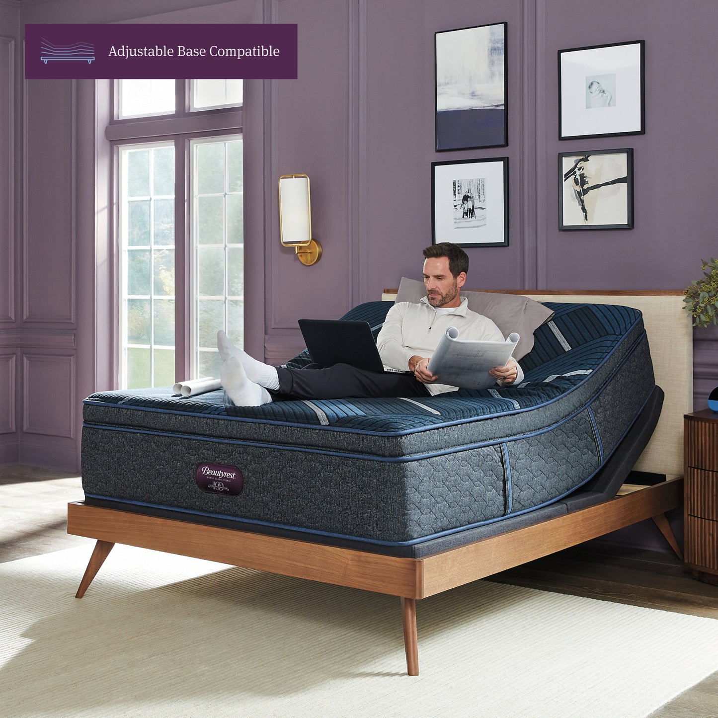 Man working on his laptop sitting on a Beautyrest World Class mattress slightly elevated on an adjustable base sitting in a brown bed frame