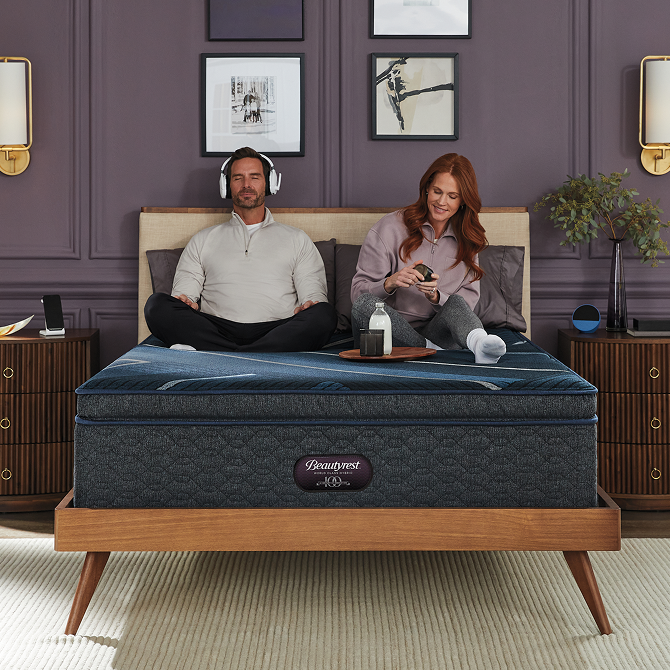 Man and woman sitting in bed on a Beautyrest World Class Mattress sitting in a brown bed frame